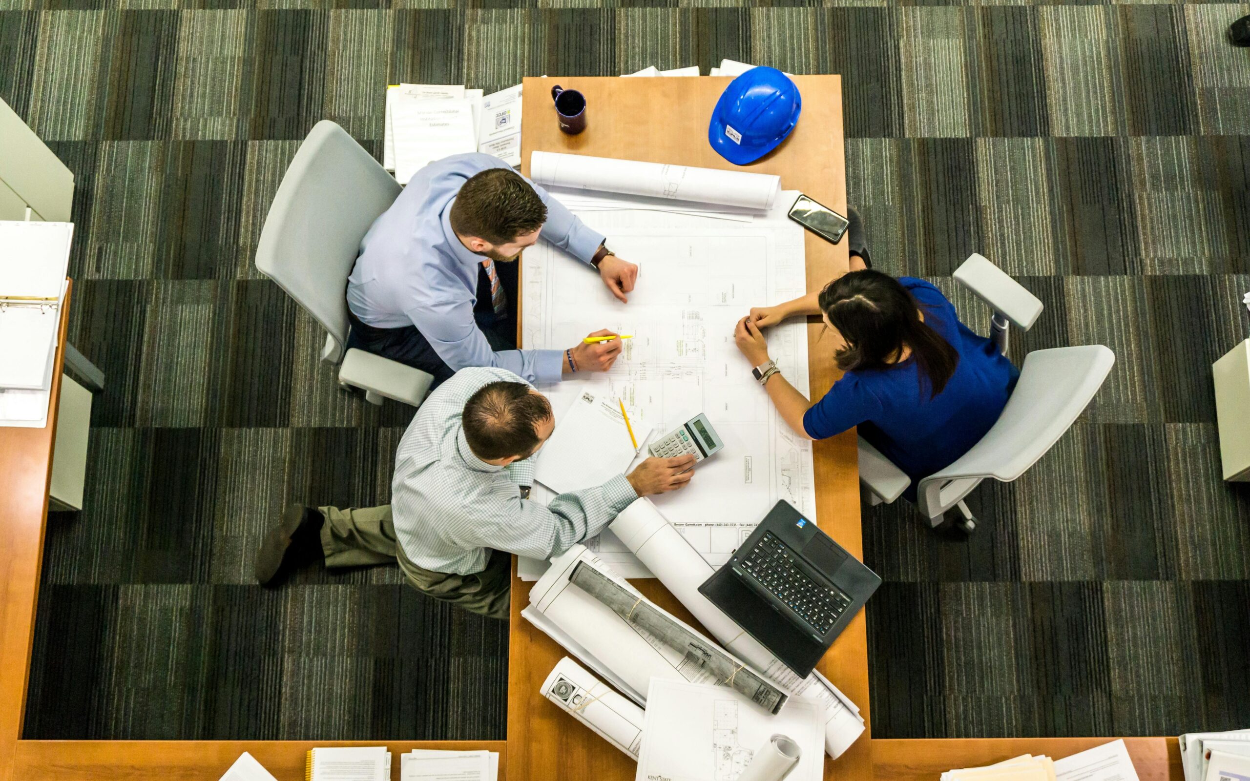 Home Top view of a team working on construction plans in an office setting.